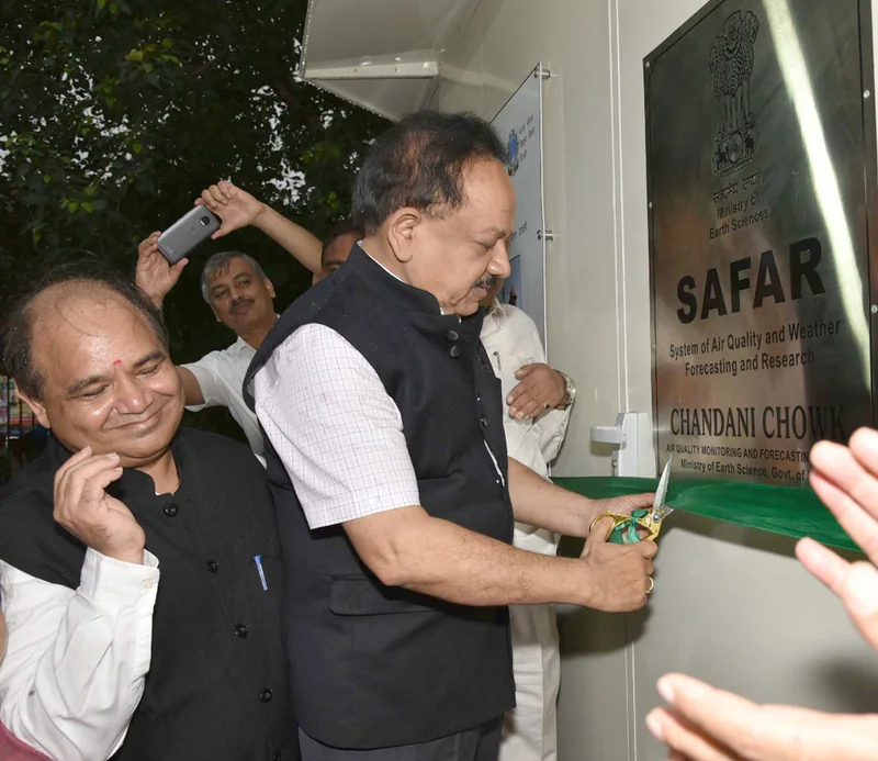 दो व्यक्ति SAFAR लिखी धातु की पट्टिका पर फीता काट रहे हैं